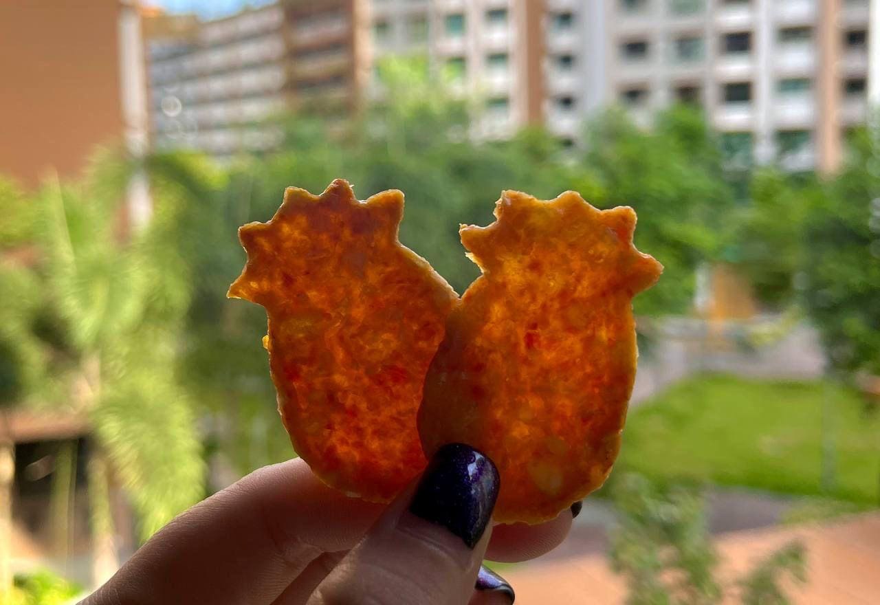 Two pineapple crisps held up against green trees