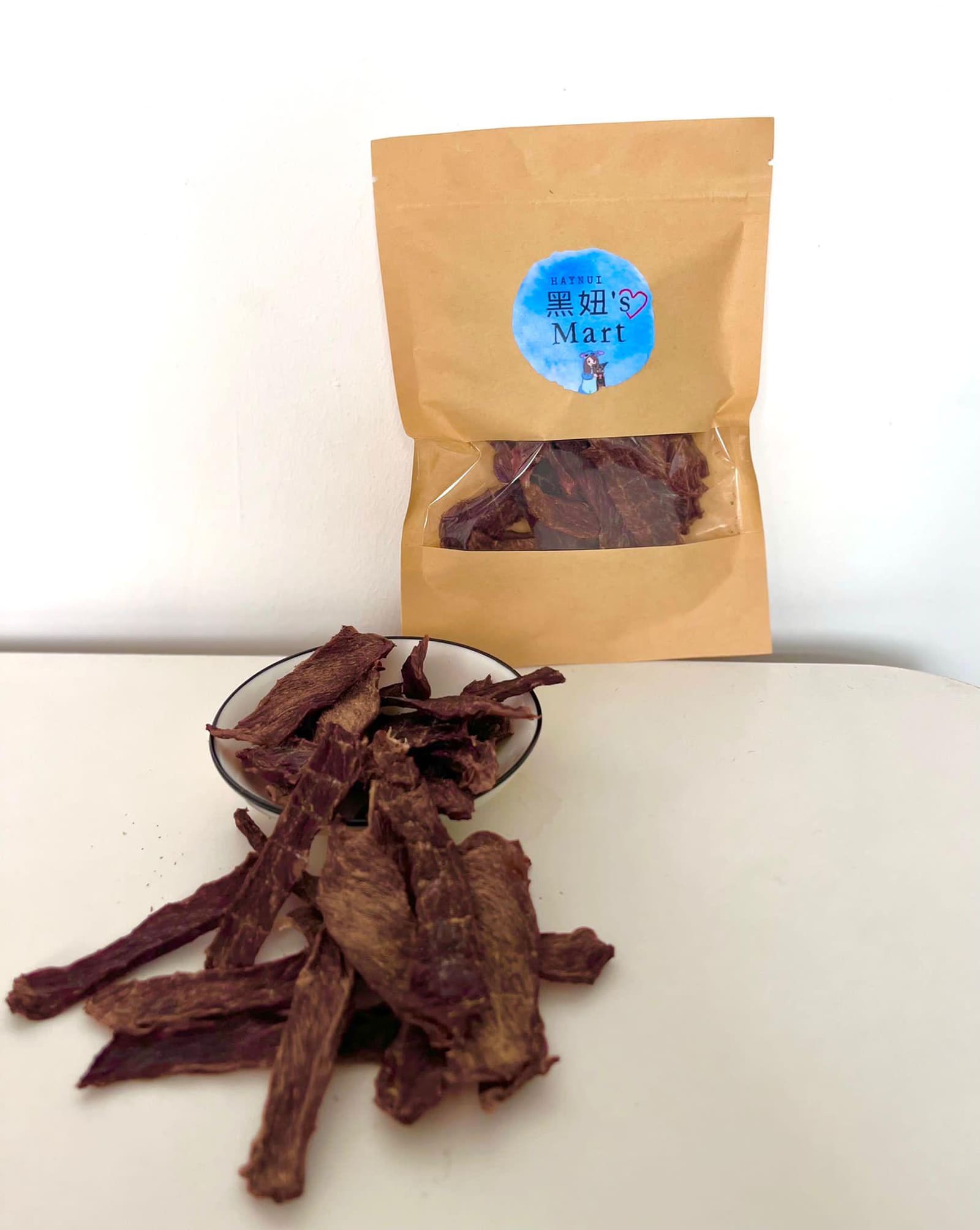 A kraft pouch of jerky beside a bowl of dark jerky strips