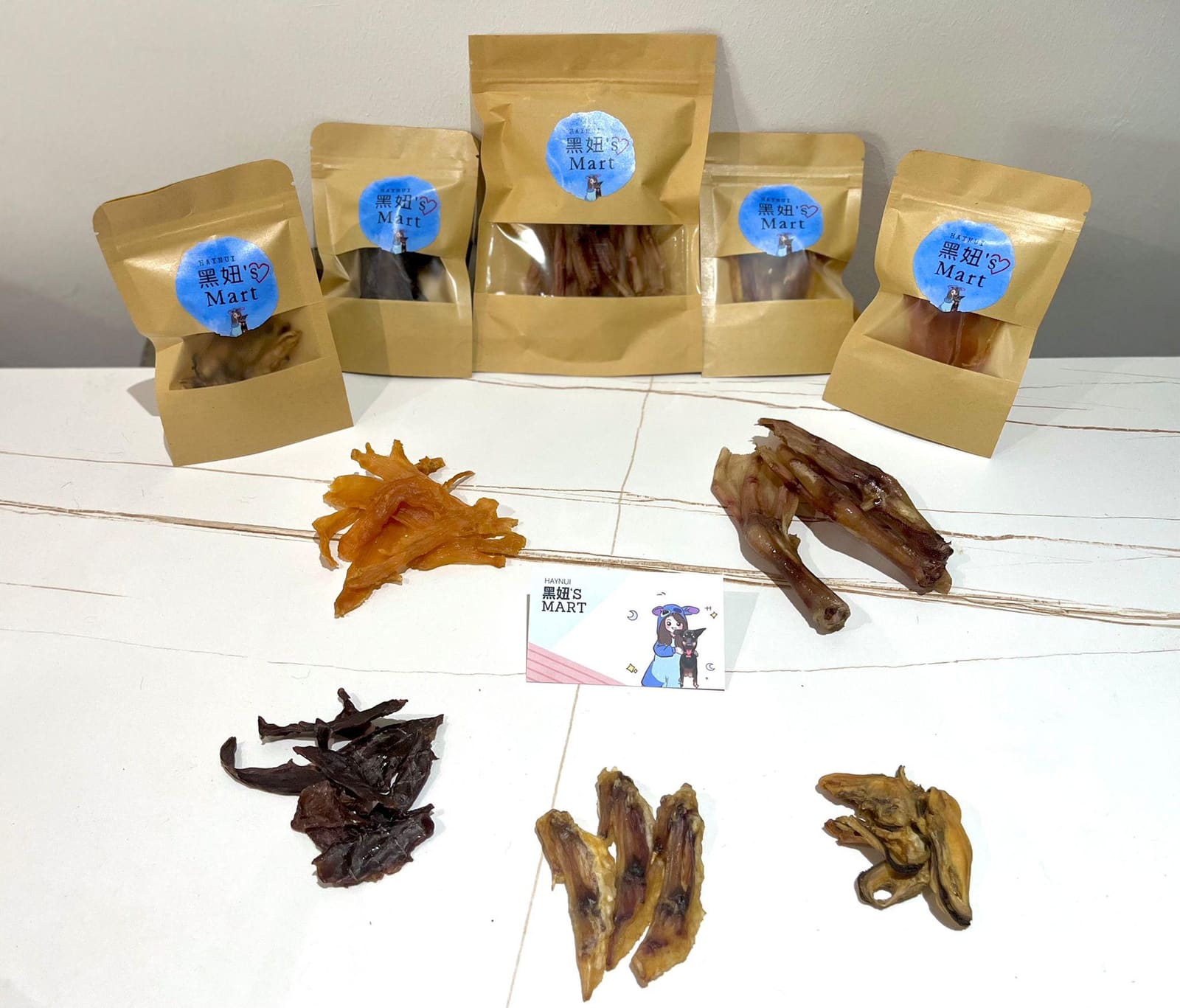 Five kraft bags with the blue 黑妞's Mart sticker, five dried treats and the name card on white marble