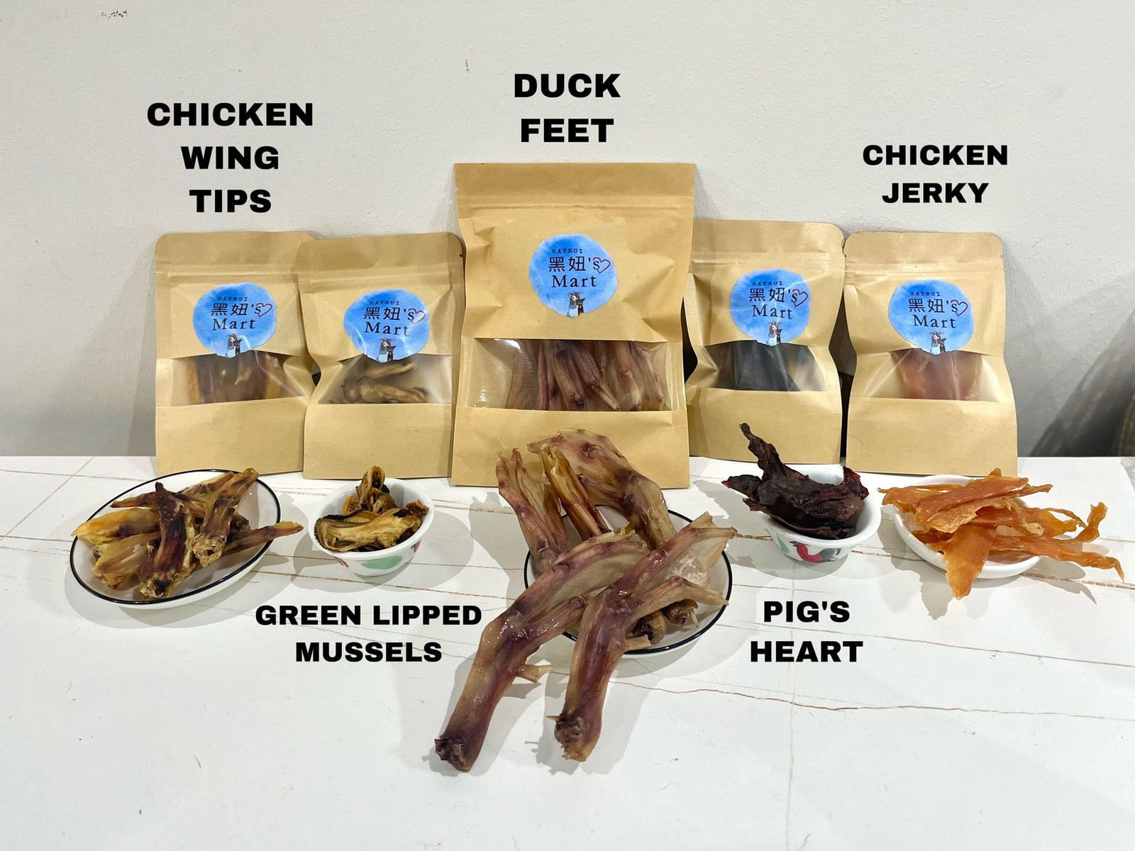 The five dried treats in bowls in front of their kraft bags, each labelled by name