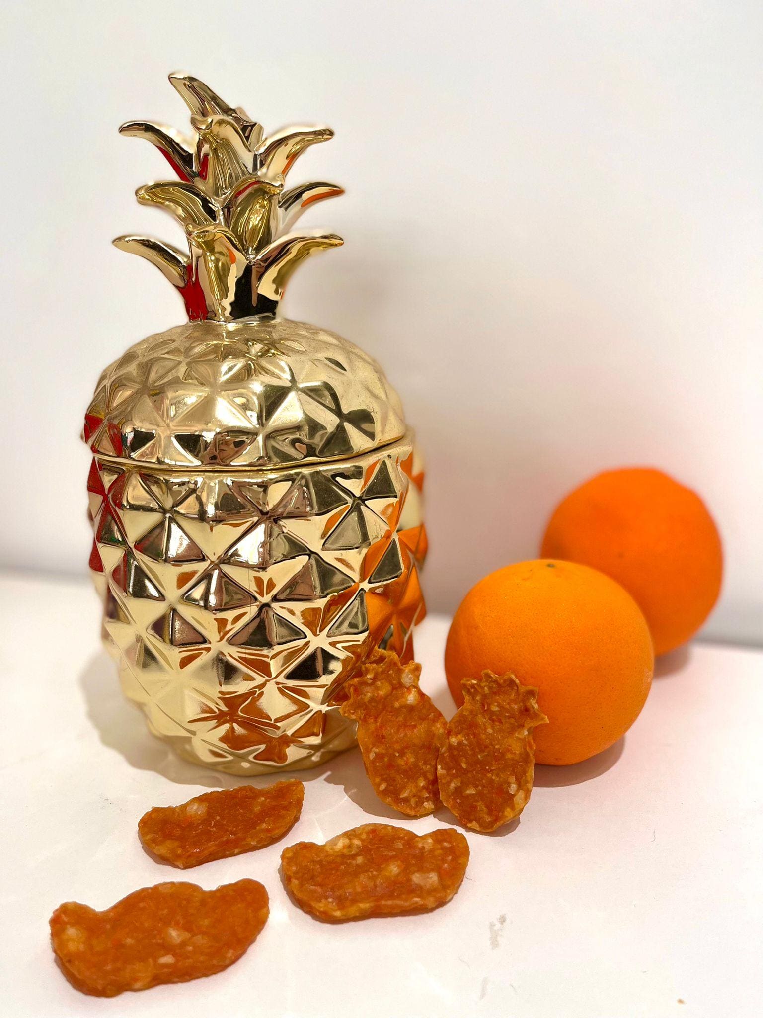 Pineapple shaped crisps beside a gold pineapple jar and two oranges